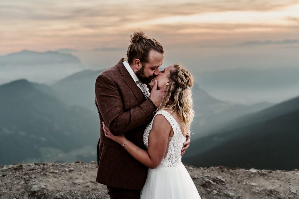 Wedding couple in the dolomites during their elopement. The man is kissing his bride while he holds her head
